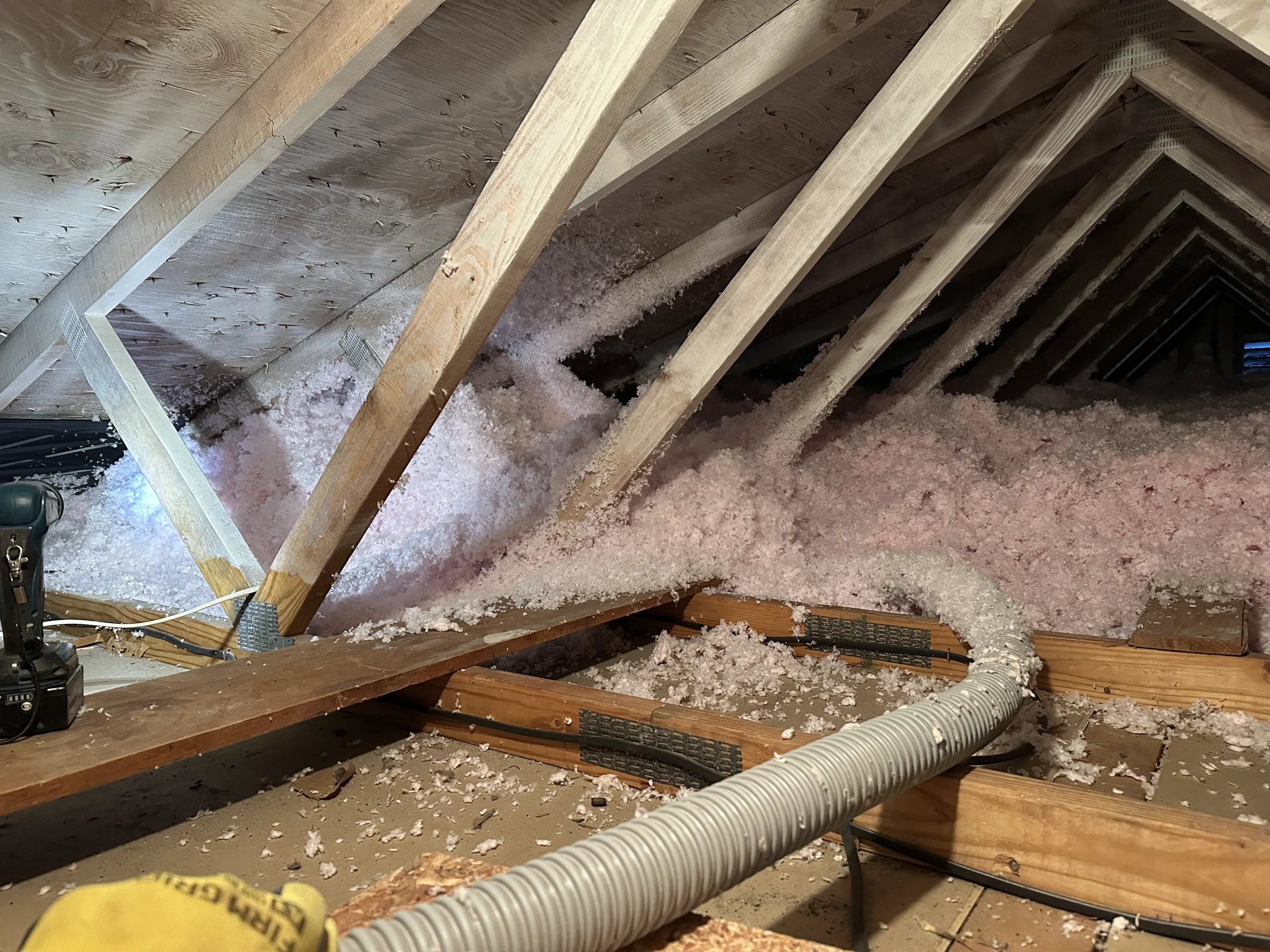 Attic with blown-in pink insulation, exposed wooden rafters and installation hose Insulation