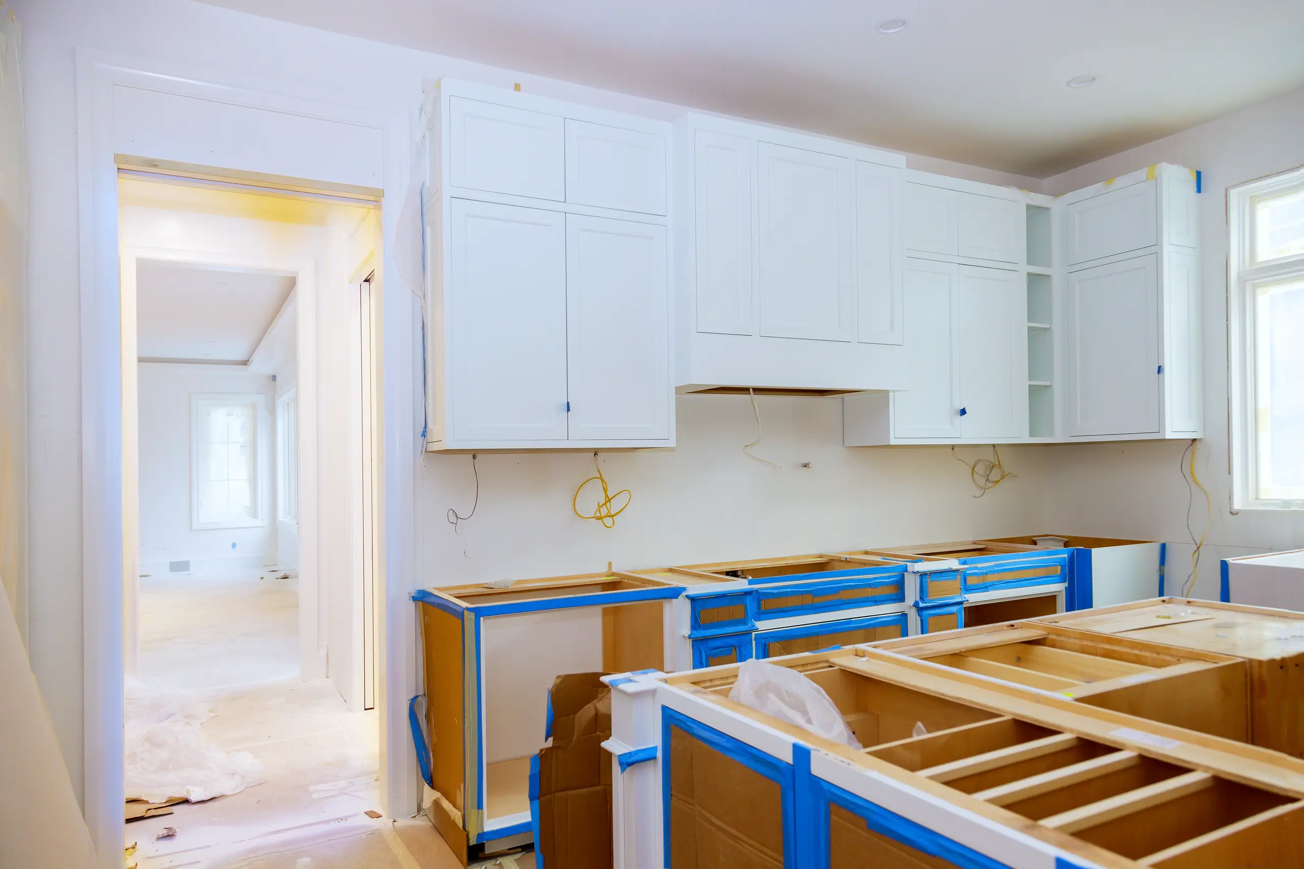 Kitchen interior mid-renovation with white upper and lower cabinets and protective tape during Kitchen Cabinets Installation