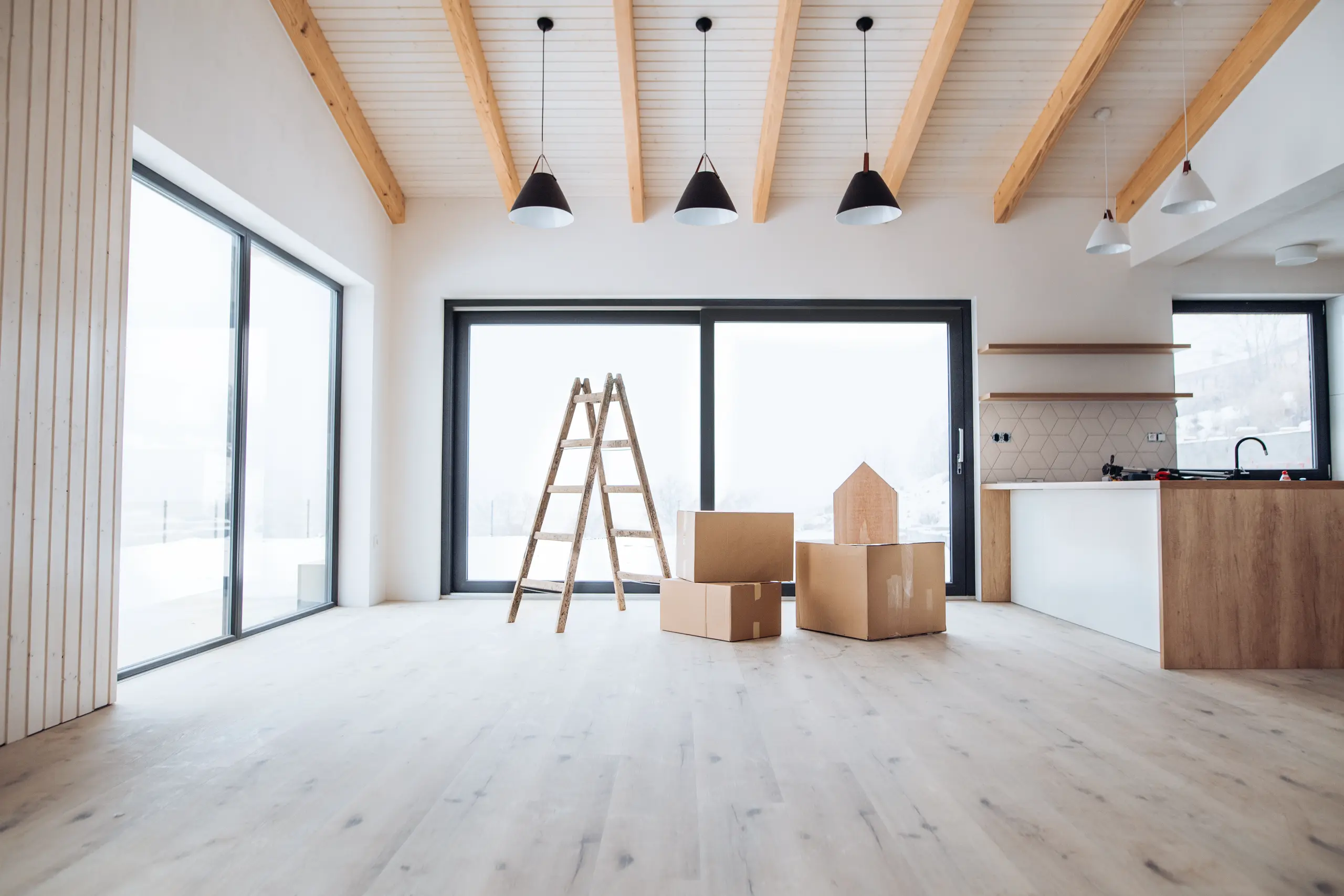 Open-concept living area with exposed wooden ceiling beams, sliding glass doors, wooden ladder and moving boxes Full Home Remodel