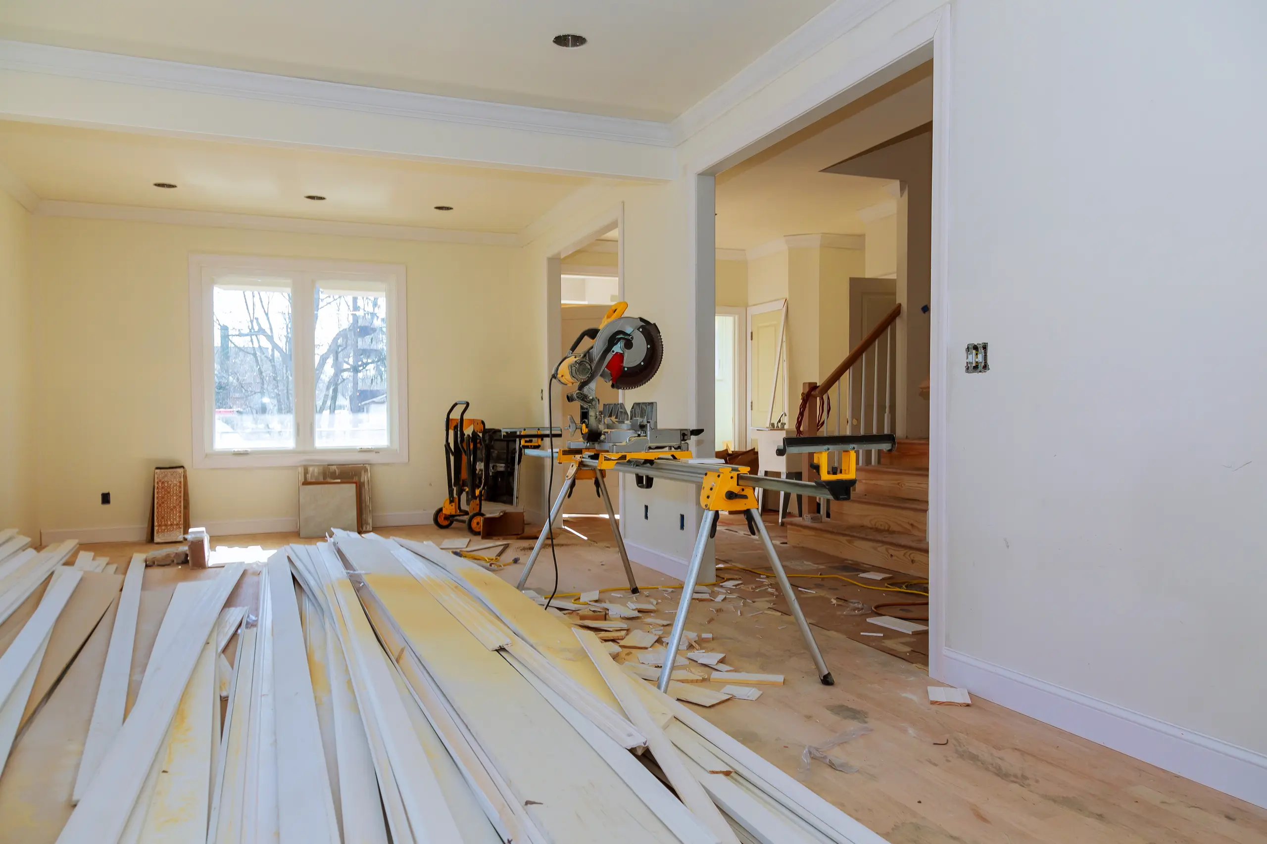 Miter saw on stand with stacked wood trim boards and scattered debris in living space during Trim Work