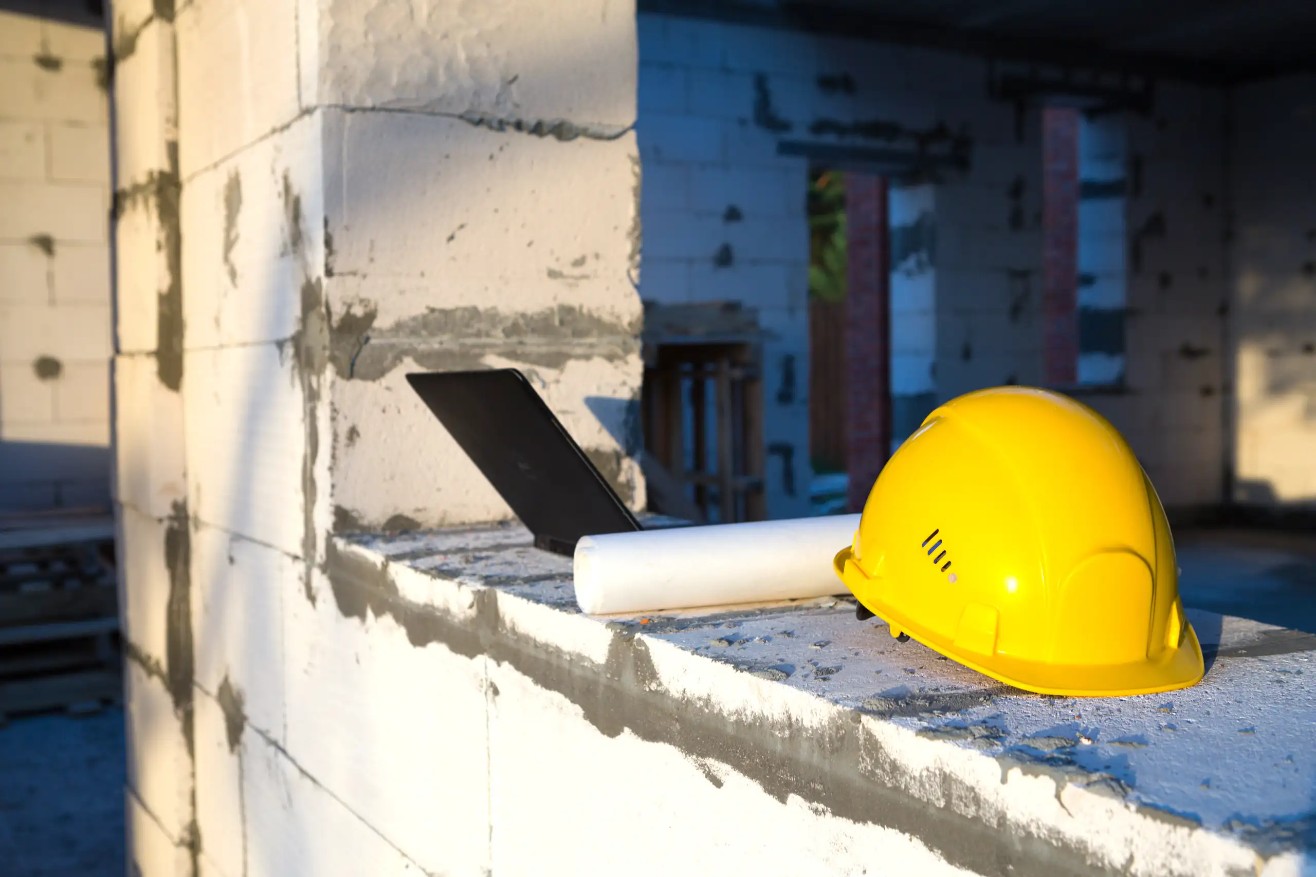 Yellow hard hat and rolled blueprint on unfinished block wall during Structural Framing work