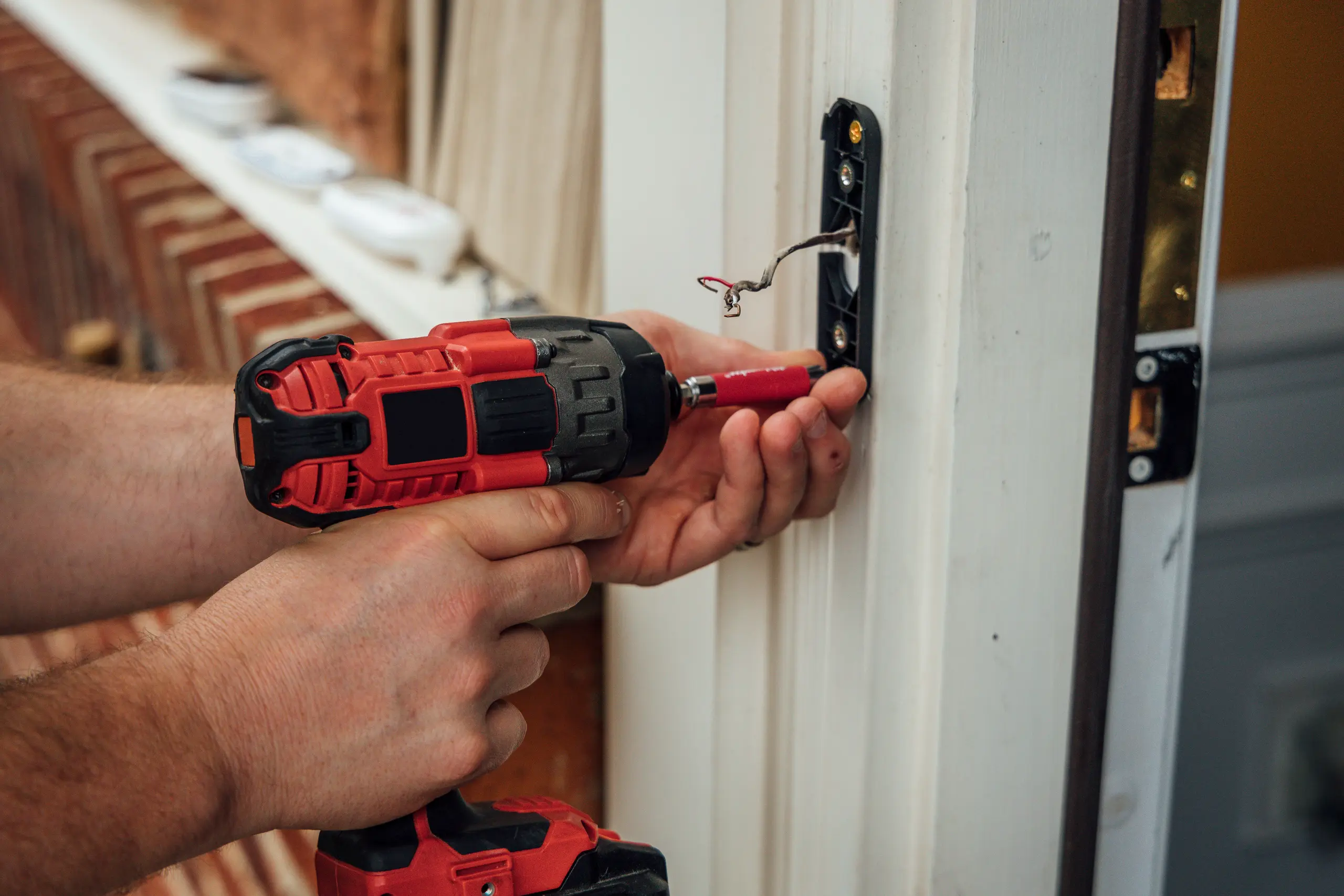 Technician securing doorbell plate with exposed wiring using a cordless drill - Electrical