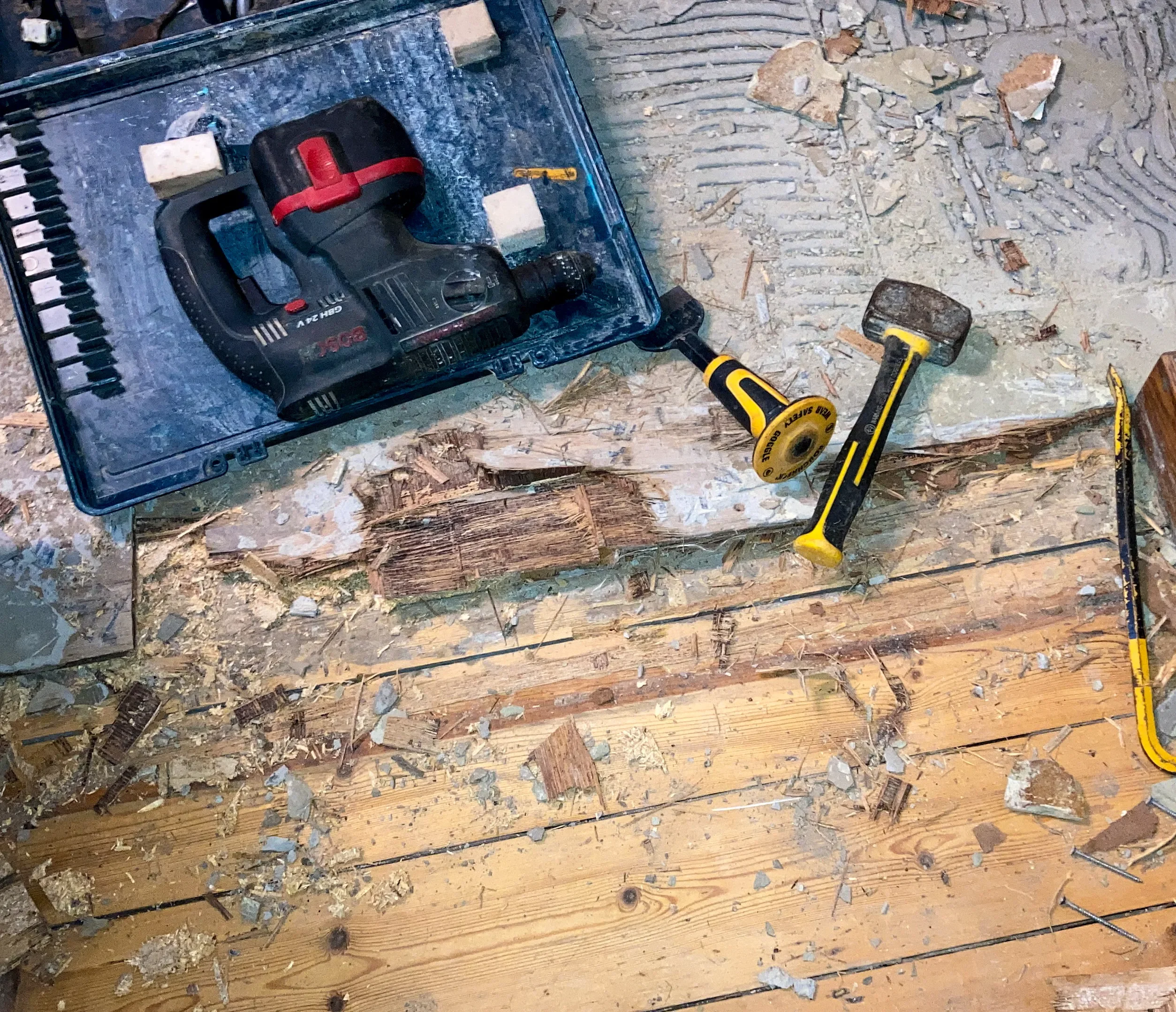 Power drill, mallet and chisel on wooden subfloor with debris during floor leveling work