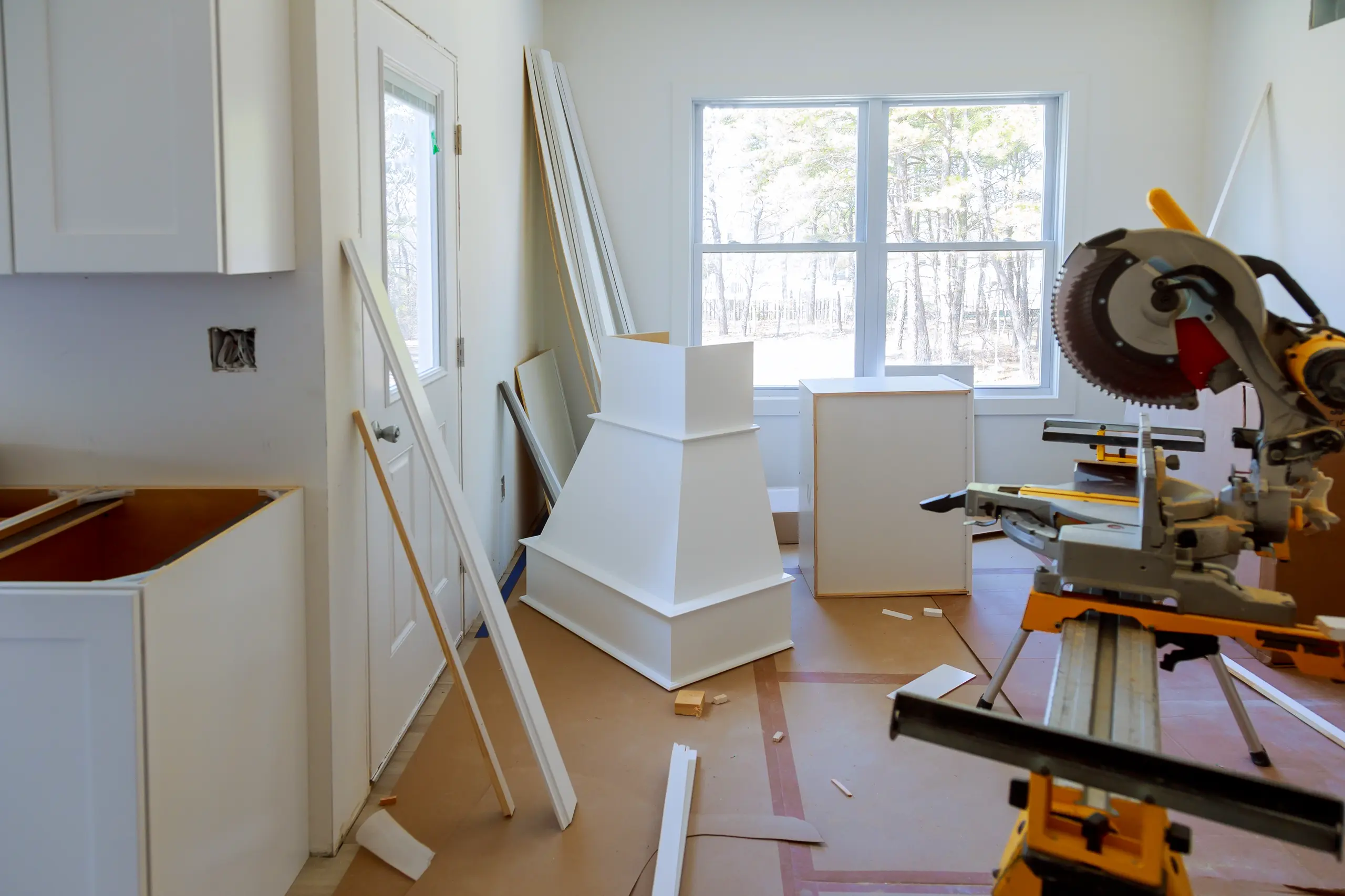 Kitchen Cabinets Installation in progress with white cabinet boxes, wood trim strips and miter saw in room
