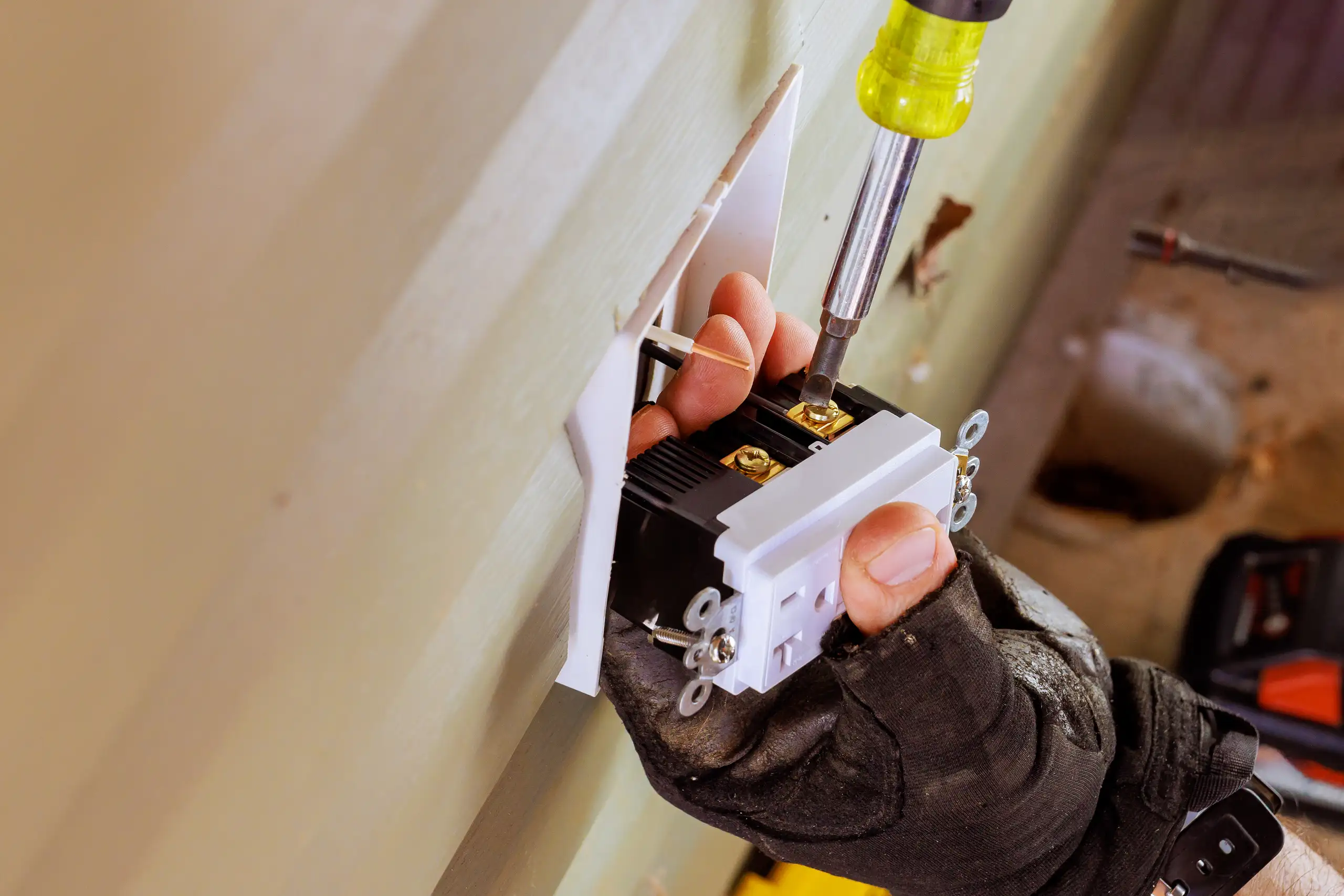 Worker installing a wall outlet receptacle in drywall during Electrical service