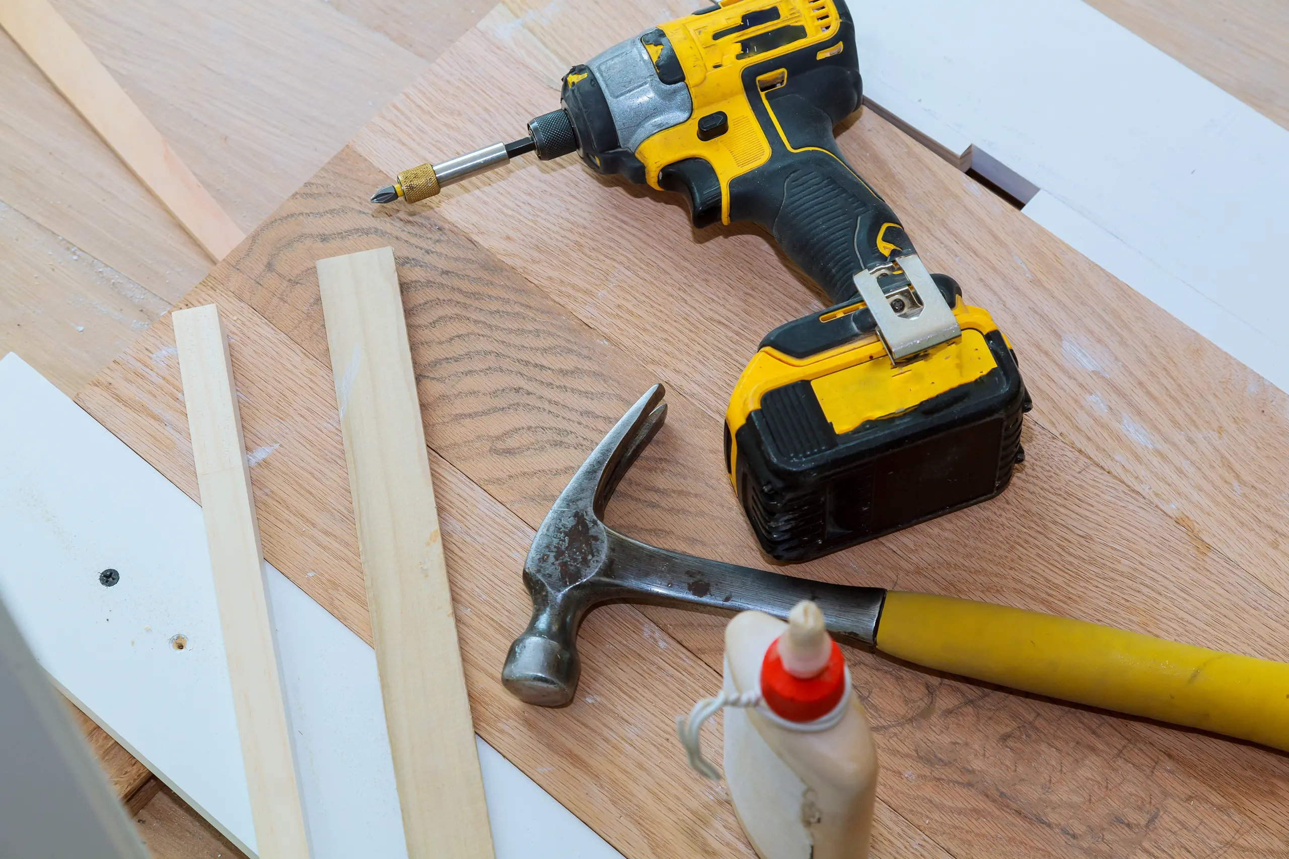Cordless drill, hammer, wood glue and hardwood trim strips on newly installed floor Floor Installation