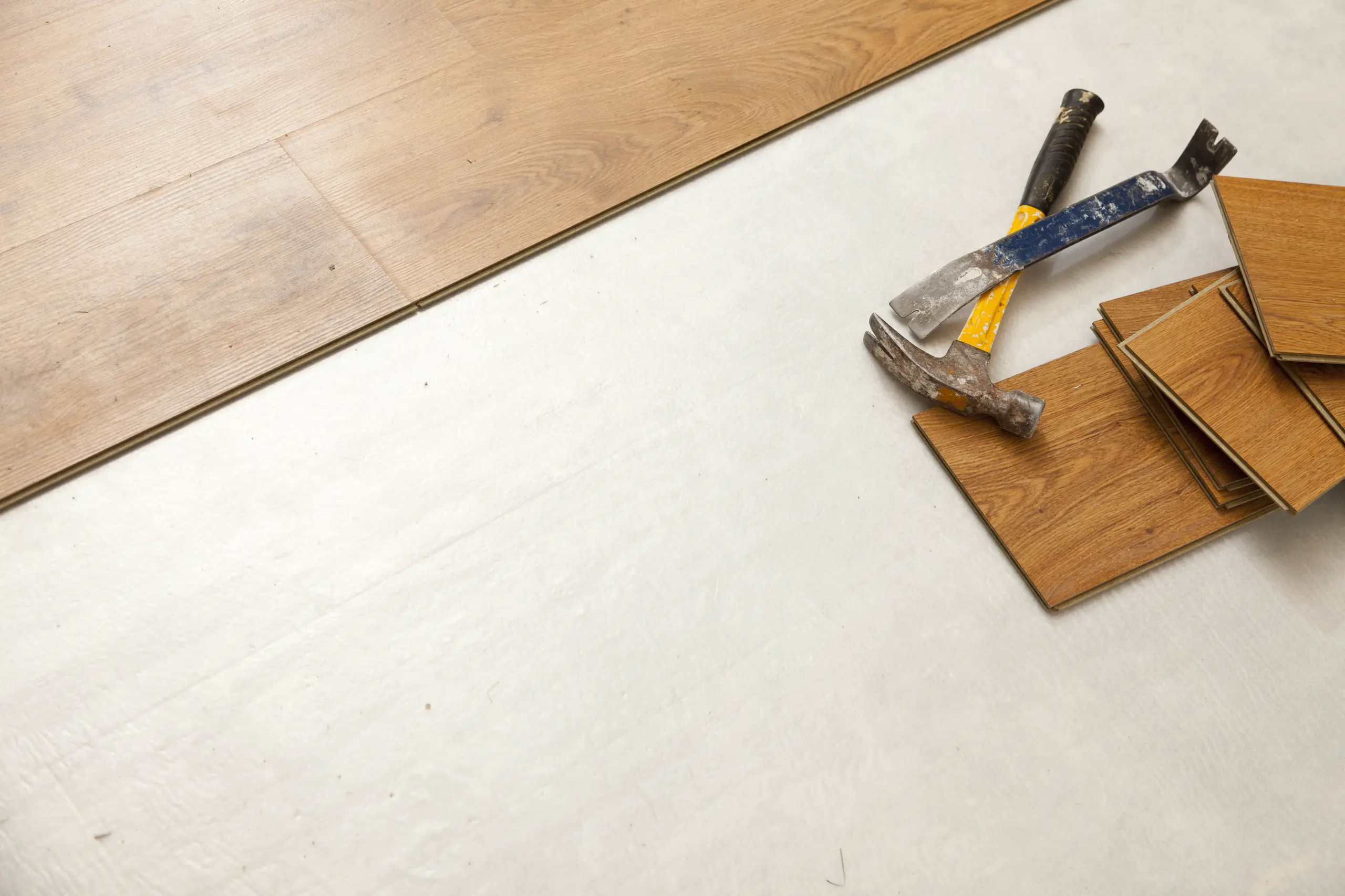 Hammer and pry bar on wood laminate planks over underlayment ready for Floor Installation