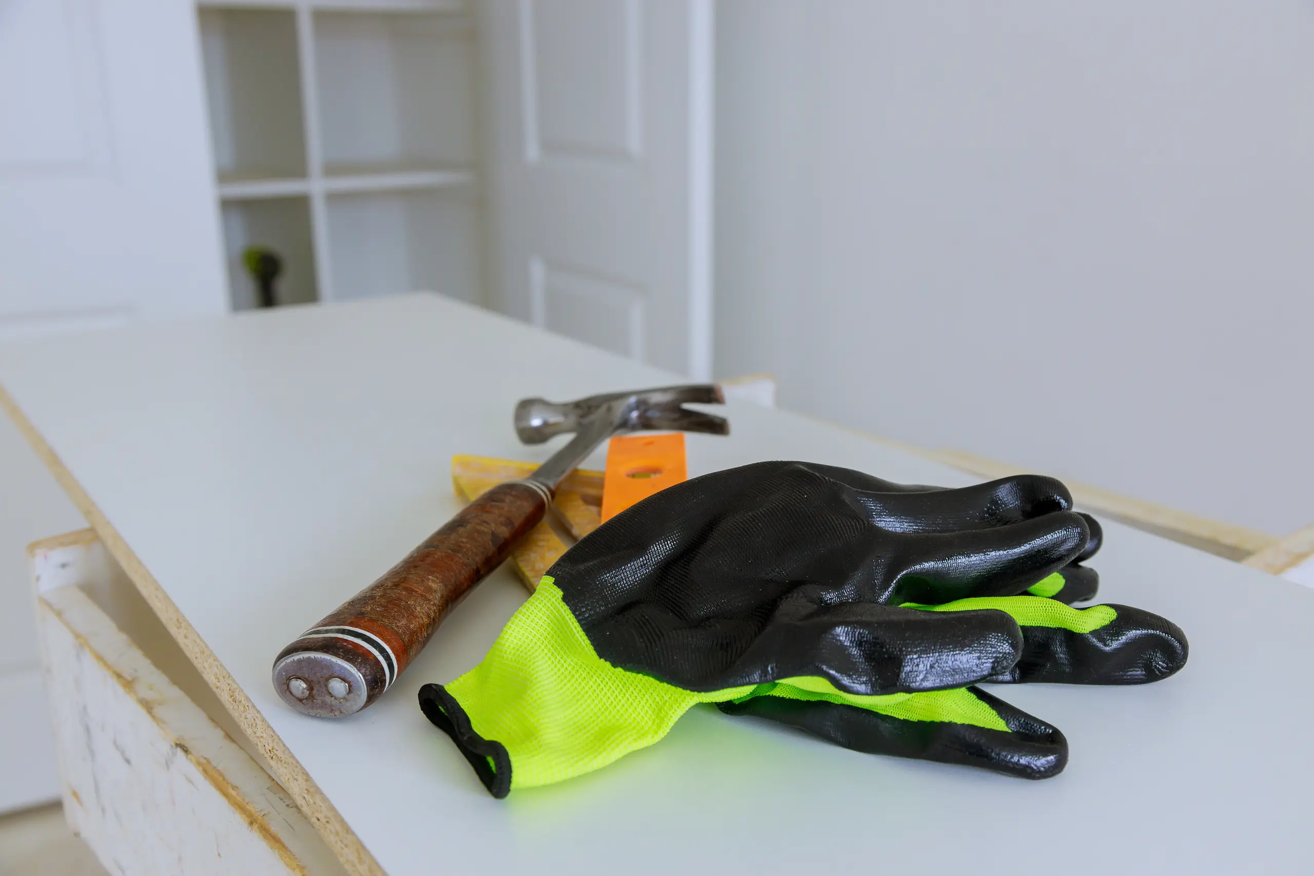 Hammer, spirit level and high-visibility work gloves on renovation site countertop during Home Improvement