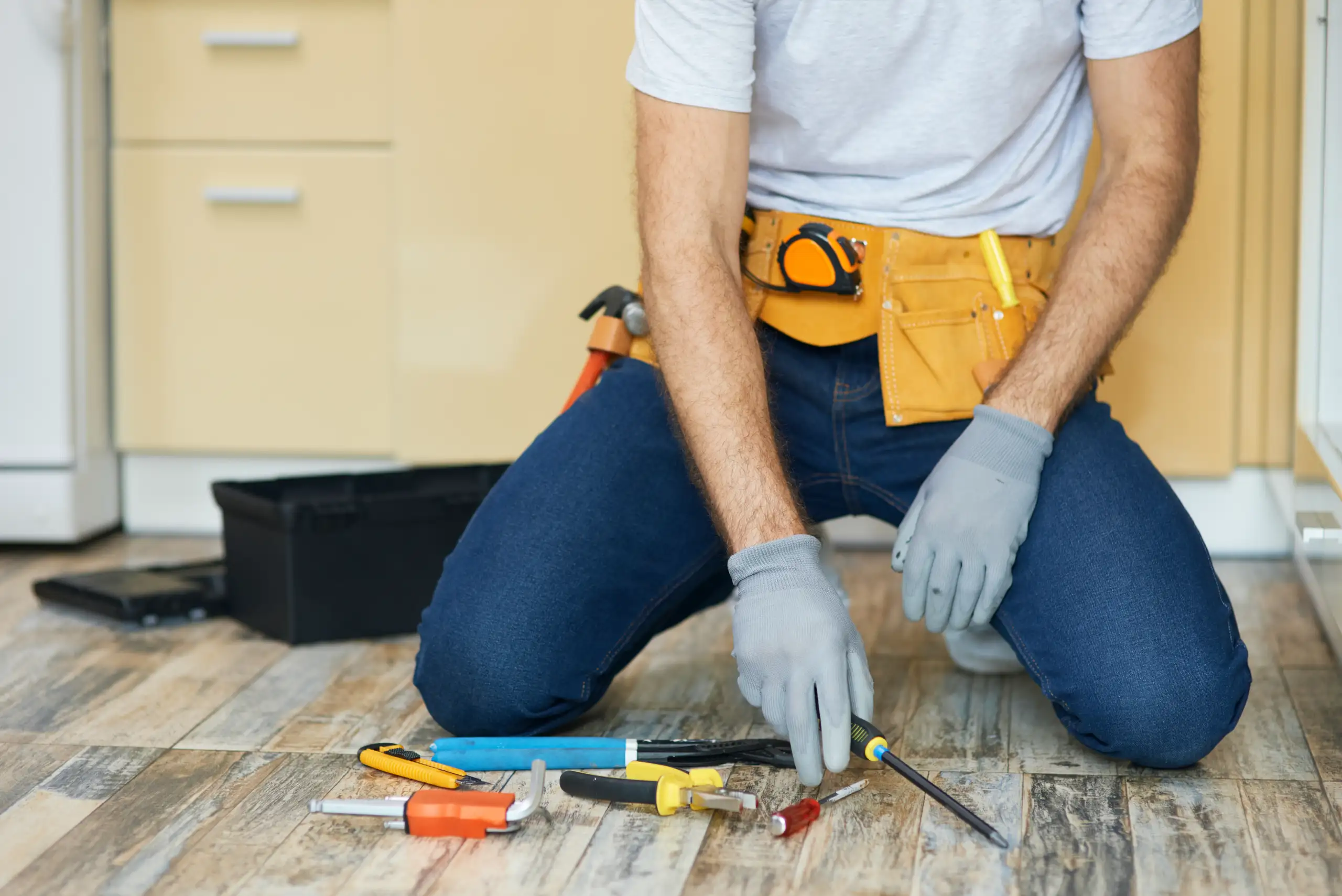 Contractor kneeling on wood floor installing planks with screwdriver and tools for Floor Installation