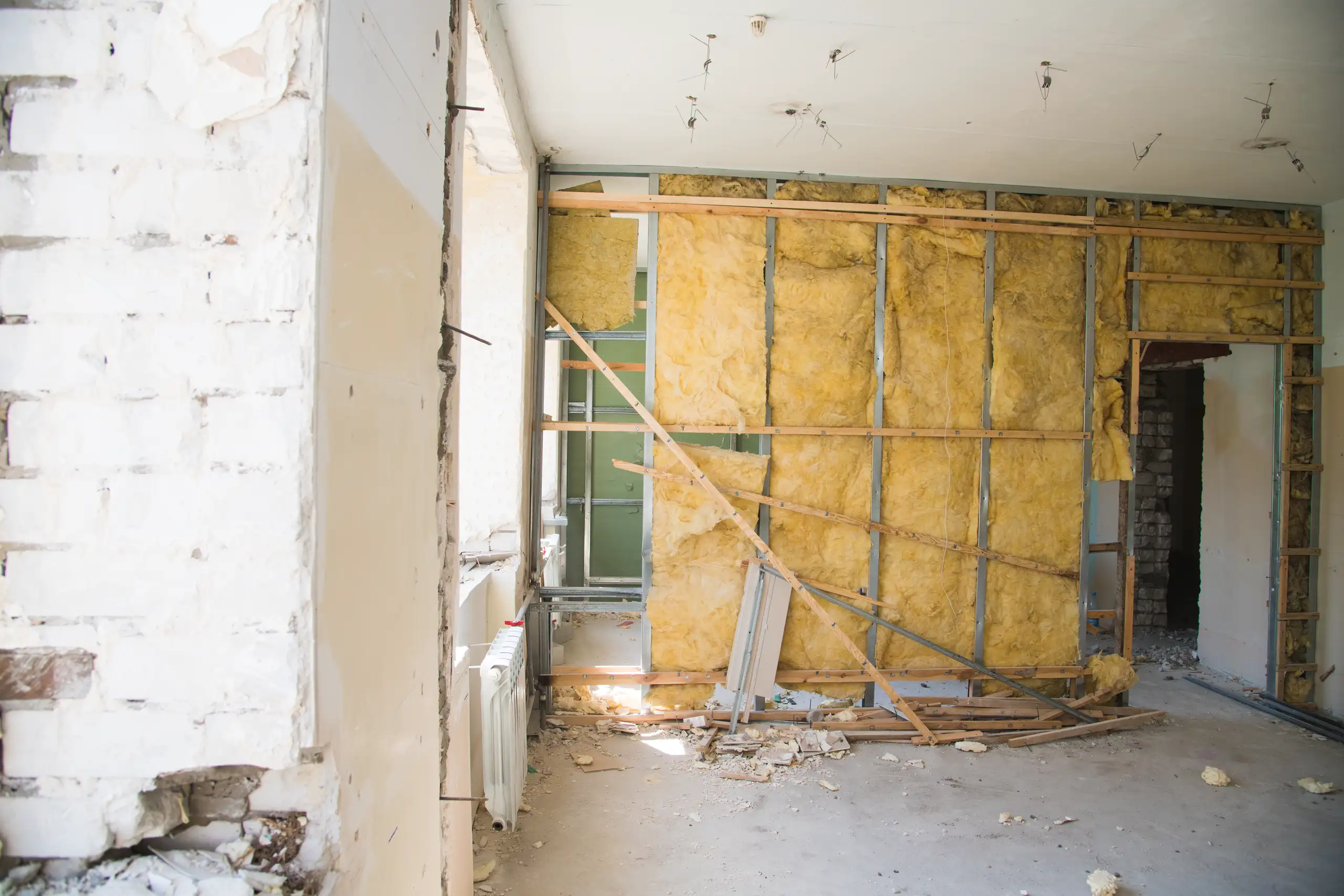 Exposed wooden studs and yellow insulation in a partially demolished interior wall under renovation, Wall Removal