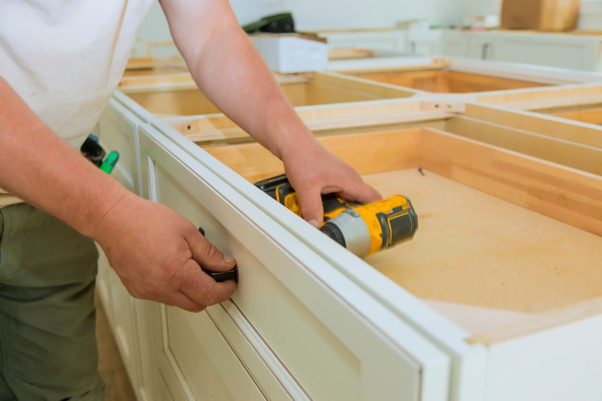 Technician installing a handle on a white kitchen cabinet drawer using a drill during Kitchen Cabinets Installation