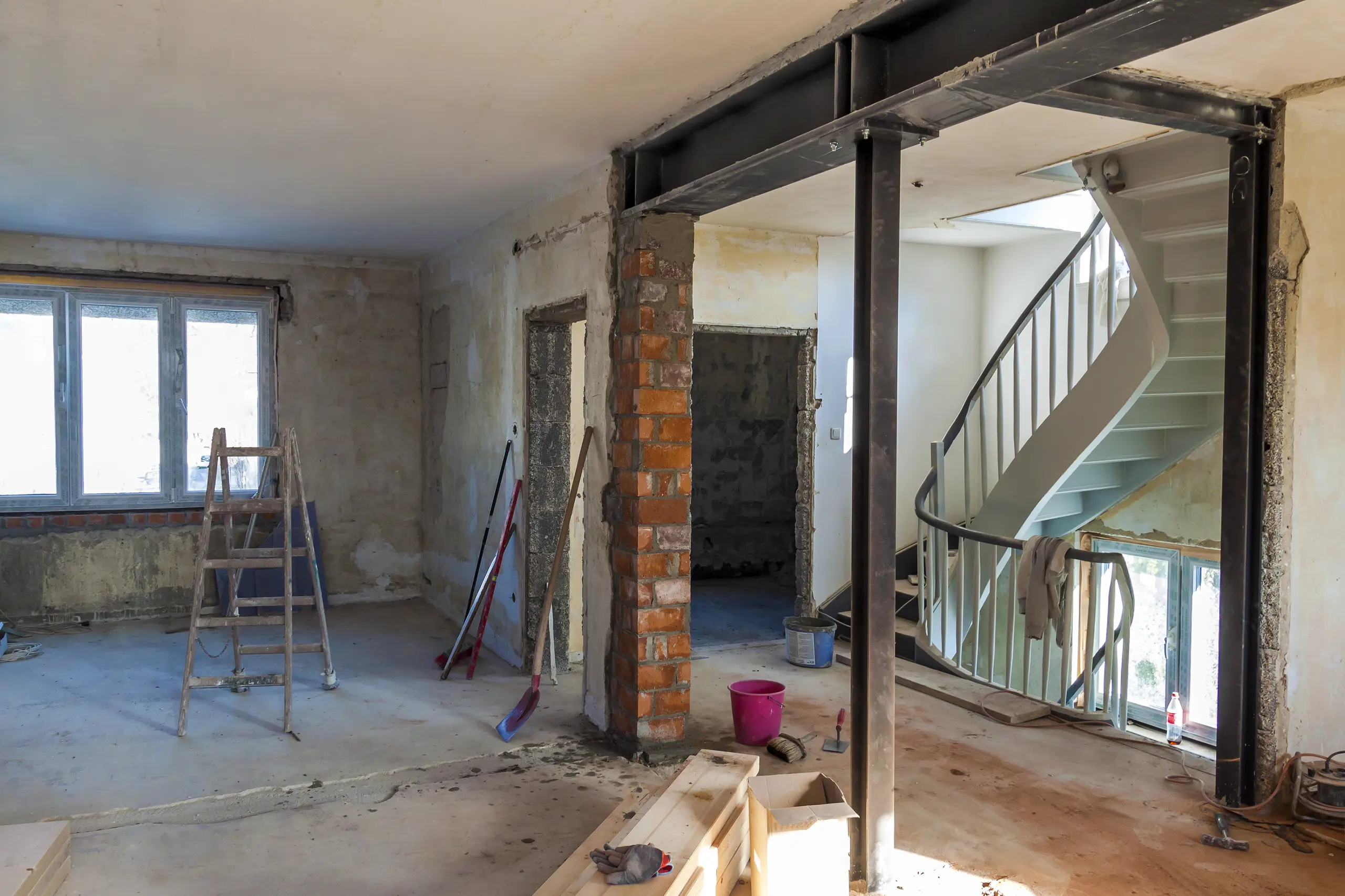 Open living space mid-renovation with exposed steel beam and brick column after load bearing wall removal