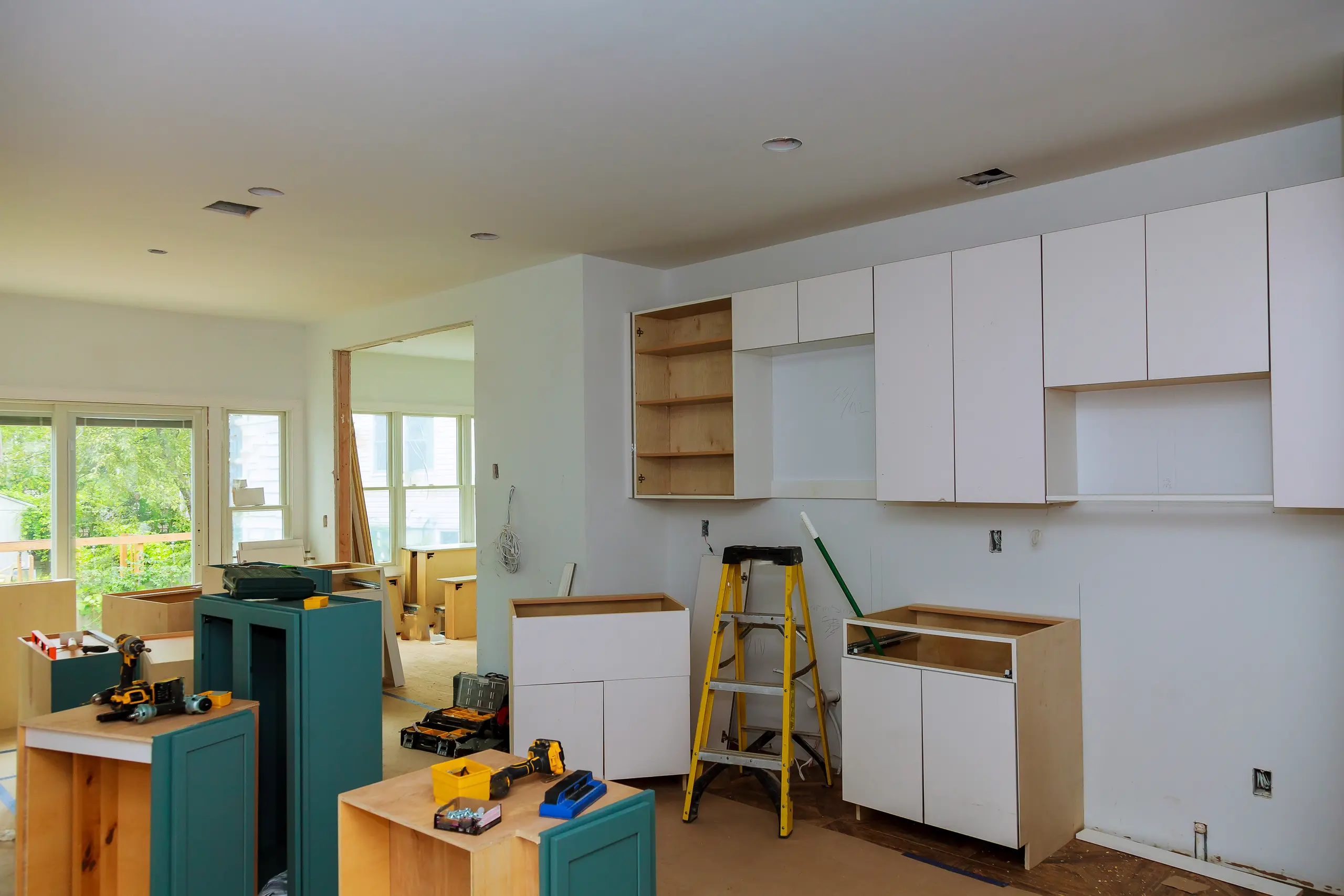 Kitchen Cabinets Installation in progress with white upper and base cabinets, scattered tools and stepladder