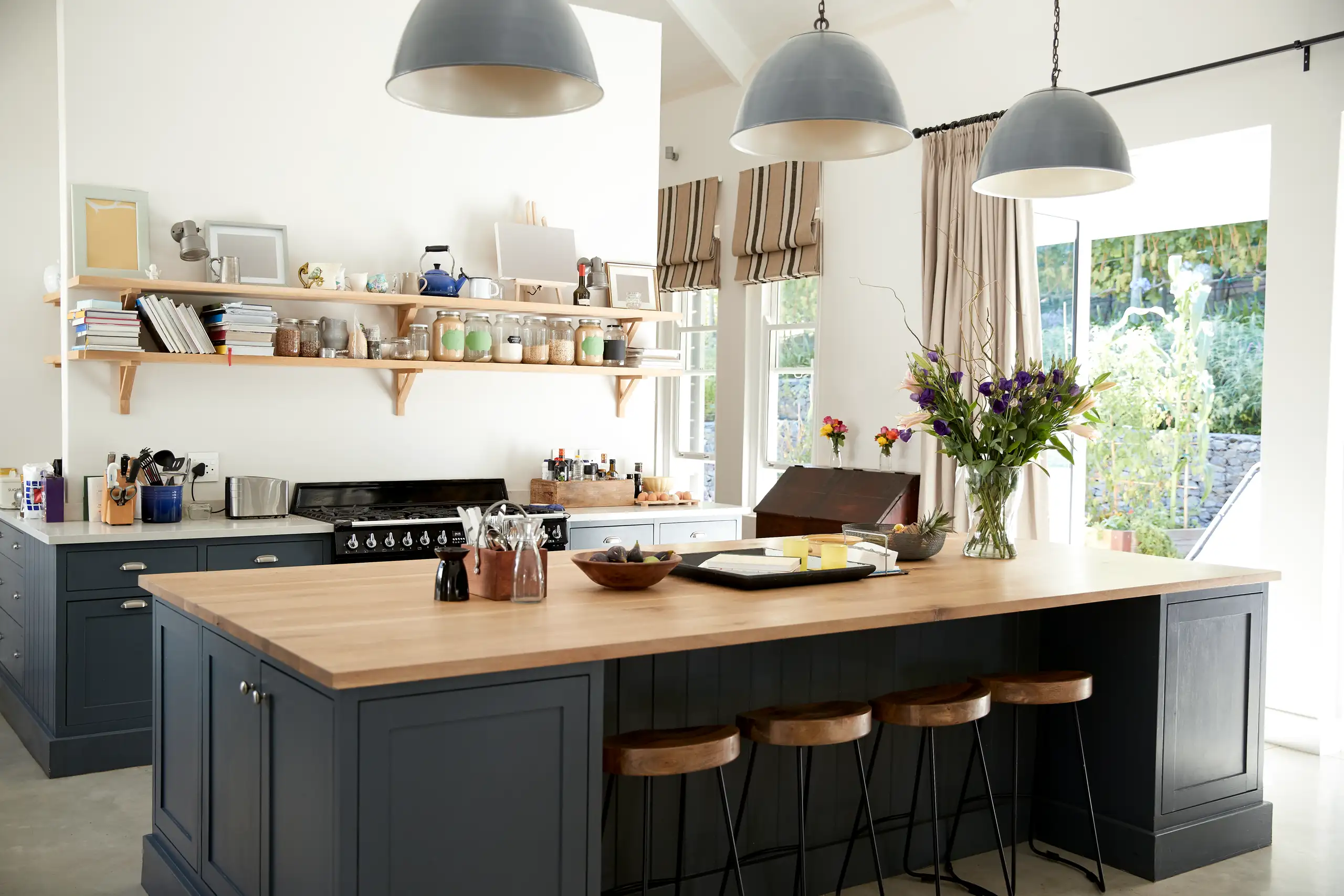 Modern kitchen after Custom Kitchen Remodel featuring a large wood-topped island, dark cabinetry, open shelves and pendant lights