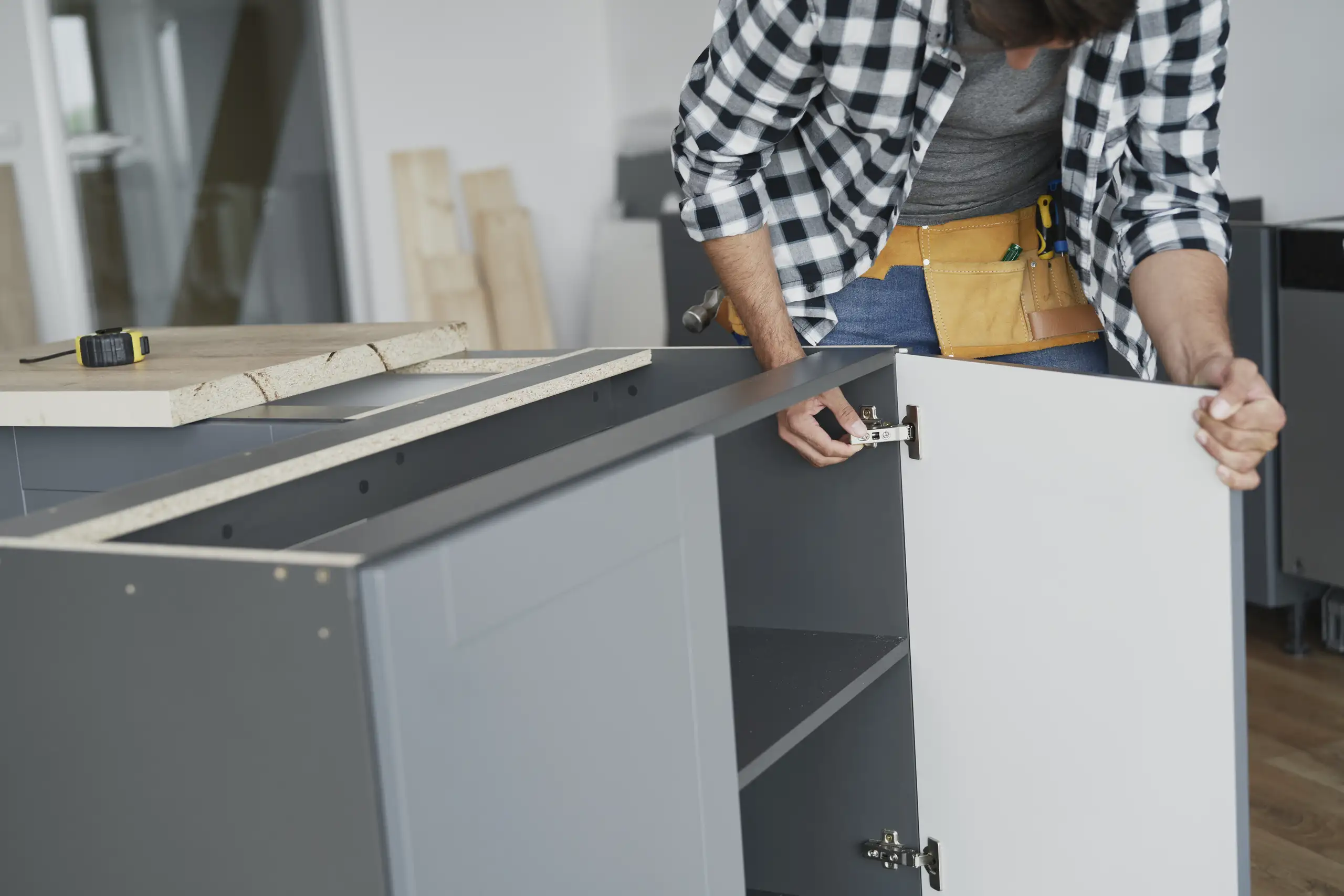 Technician installing cabinet door hinge on gray kitchen base cabinet – Kitchen Cabinets Installation