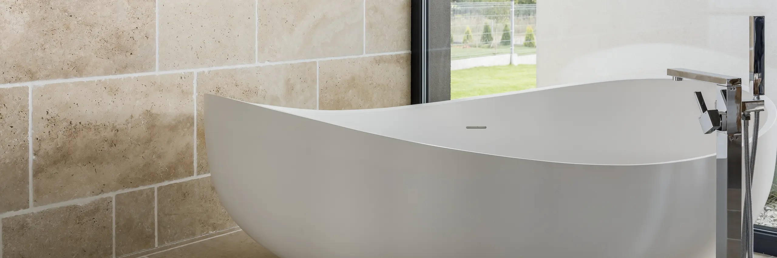 Freestanding white bathtub with chrome floor-mounted faucet and travertine wall tiles in Full Bathroom Remodel