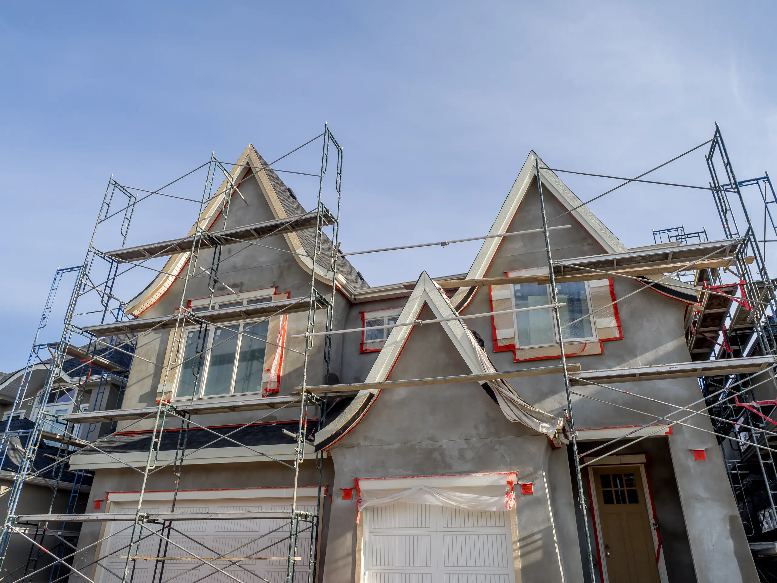 Two-story house facade with scaffolding and fresh stucco for exterior home renovation