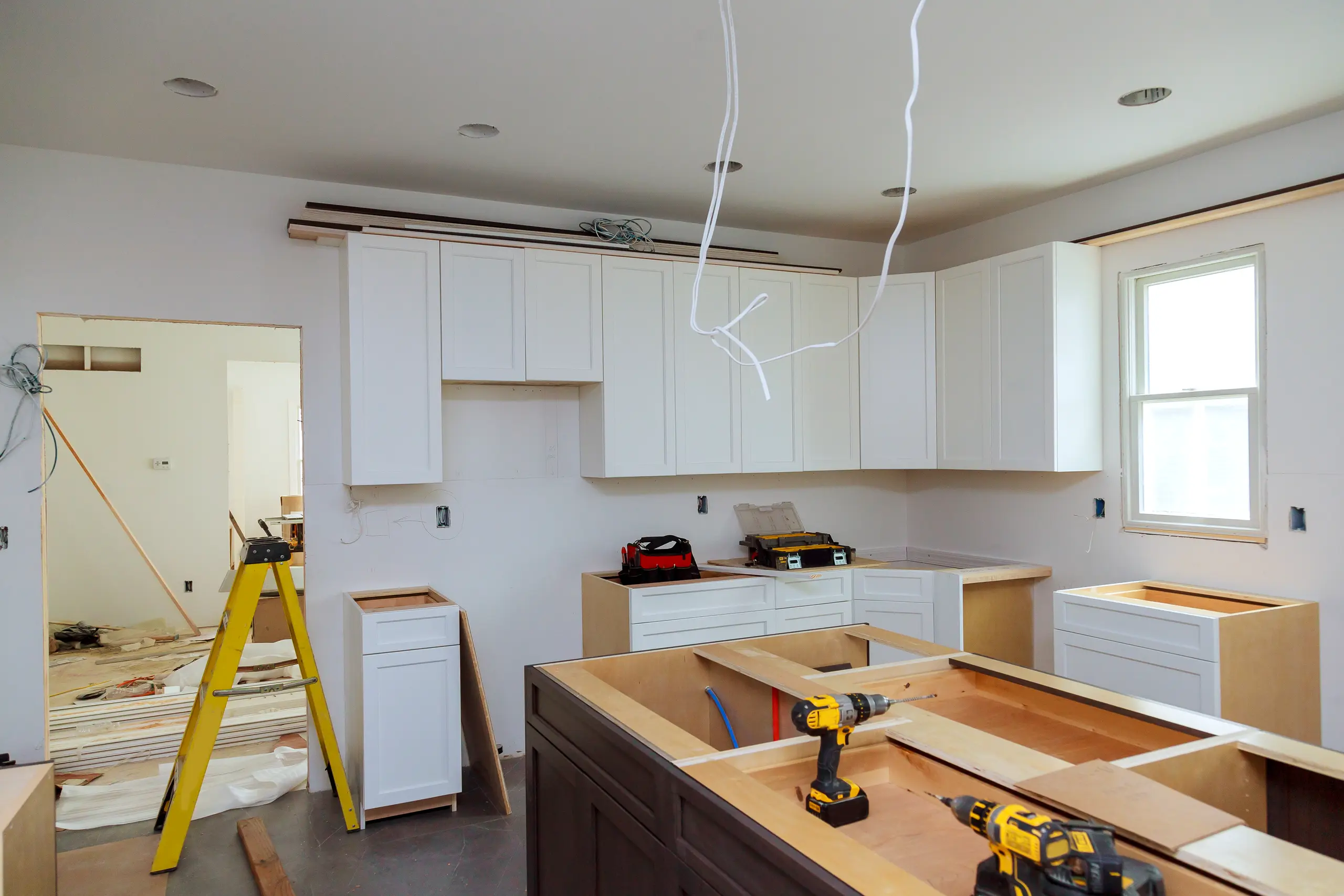 Unfinished kitchen renovation with white cabinets and island frame, drills poised for Kitchen Cabinets Installation