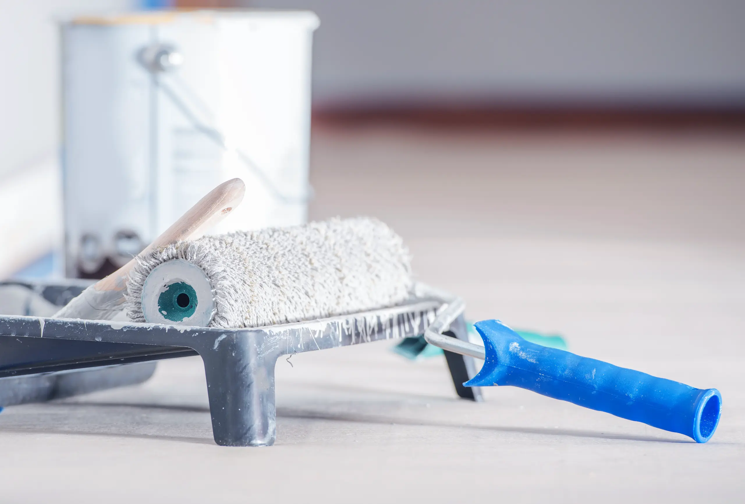 Paint roller with fresh white paint in tray and paint can in background ready for Painting