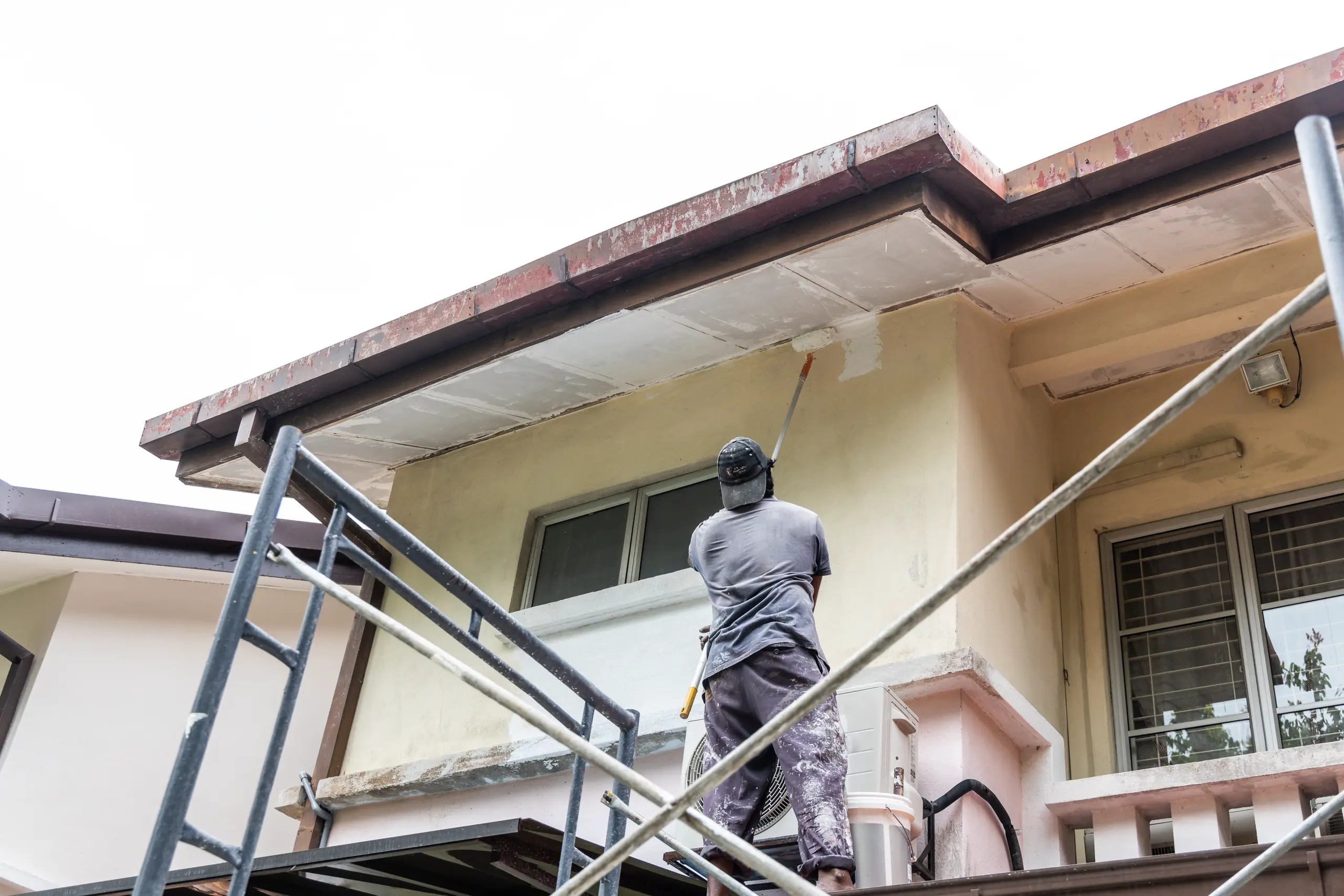 Worker on scaffolding applies paint to house soffit and fascia boards Painting