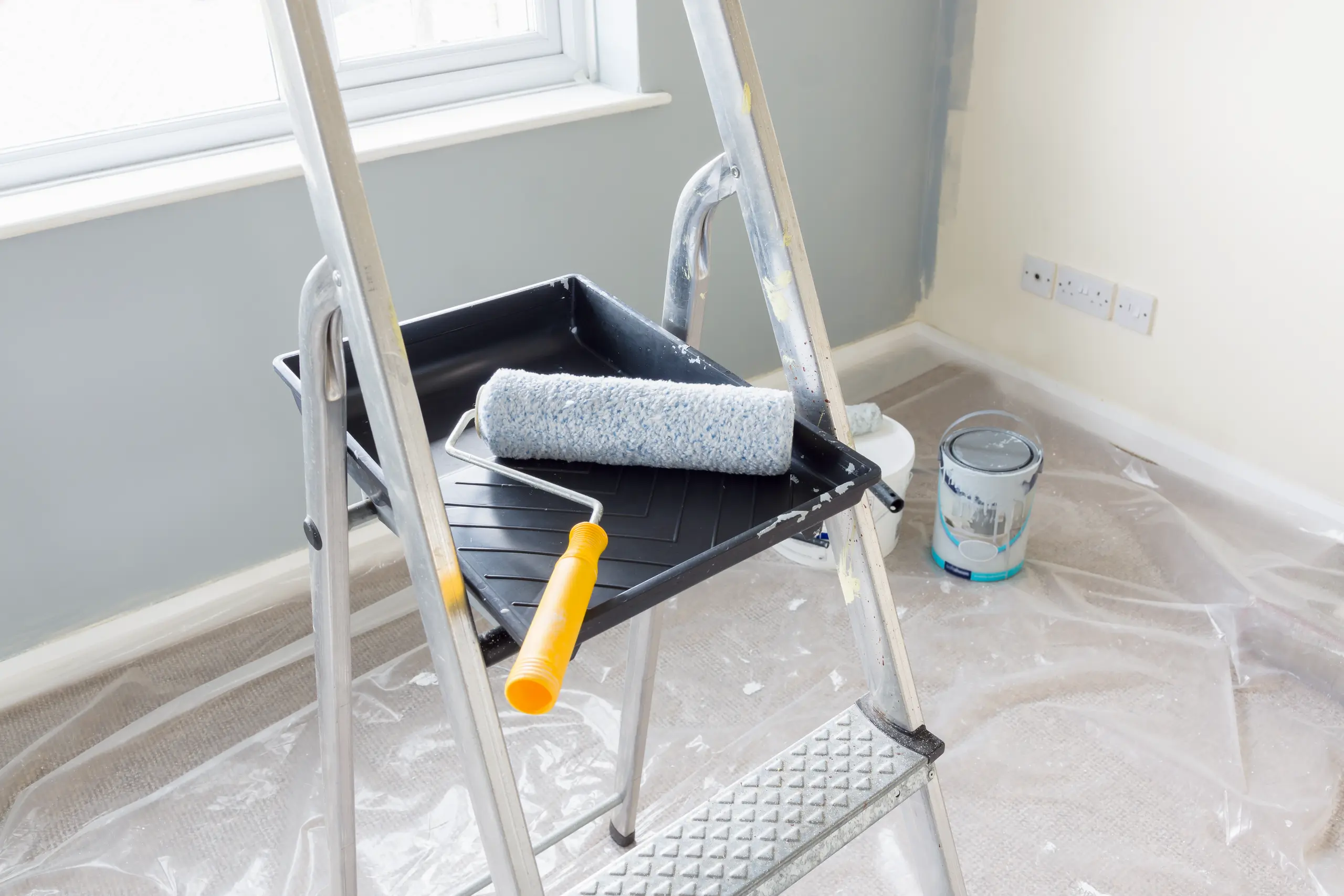 Aluminium ladder with paint tray and roller in room undergoing Painting