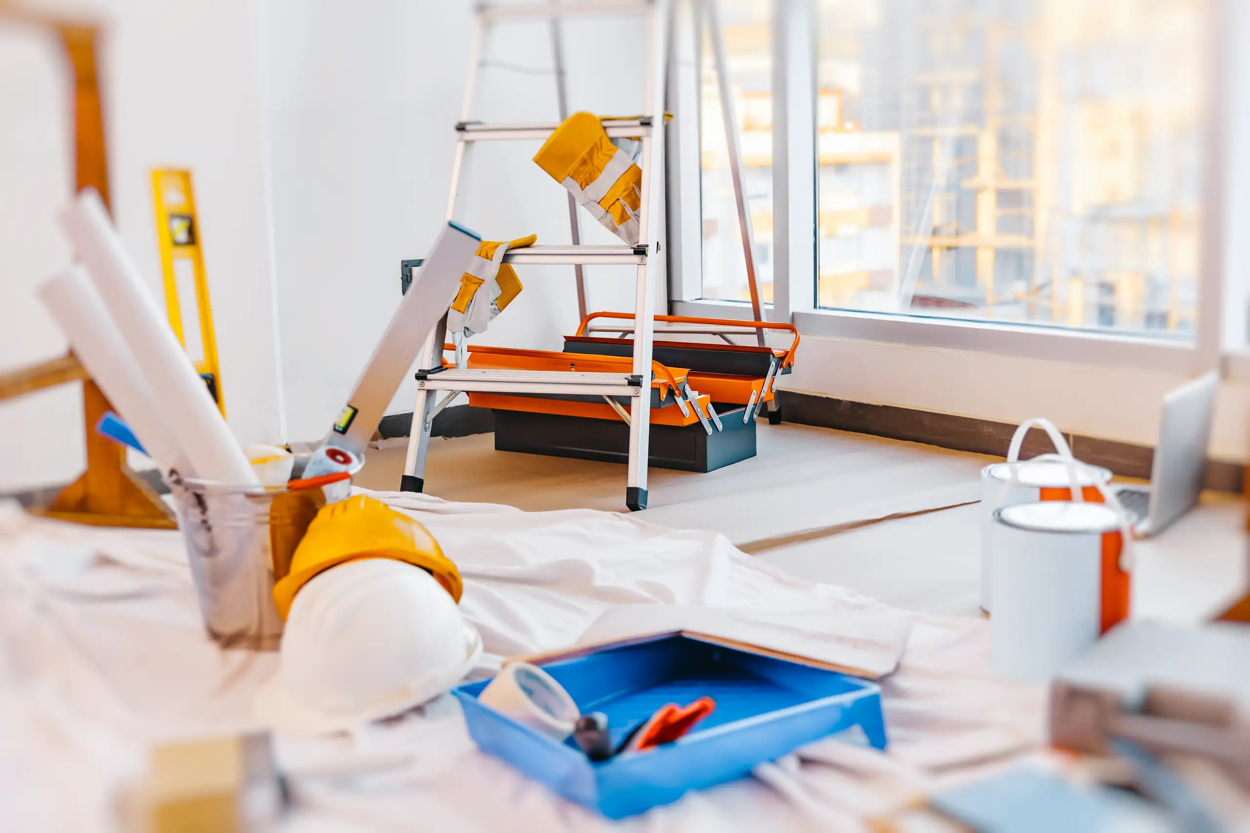 Ladder, paint trays, protective drop cloth and tools staged for interior Painting during home renovation