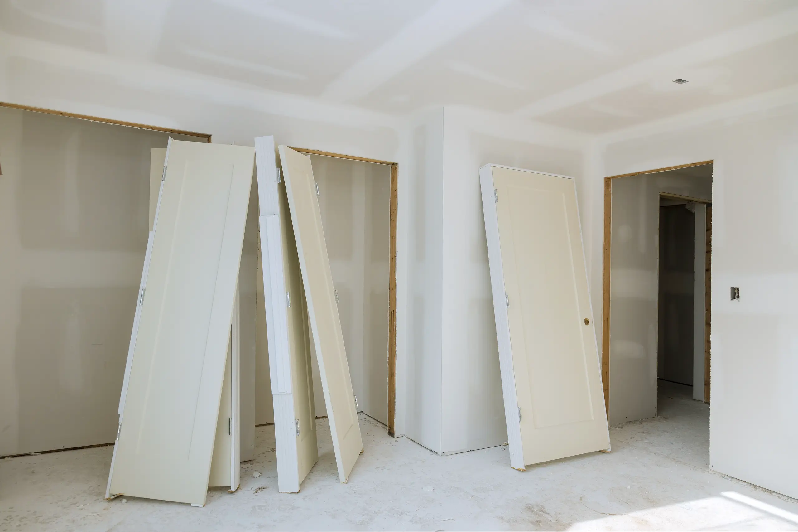 Several detached white doors leaning against unfinished drywall walls awaiting Door Installation