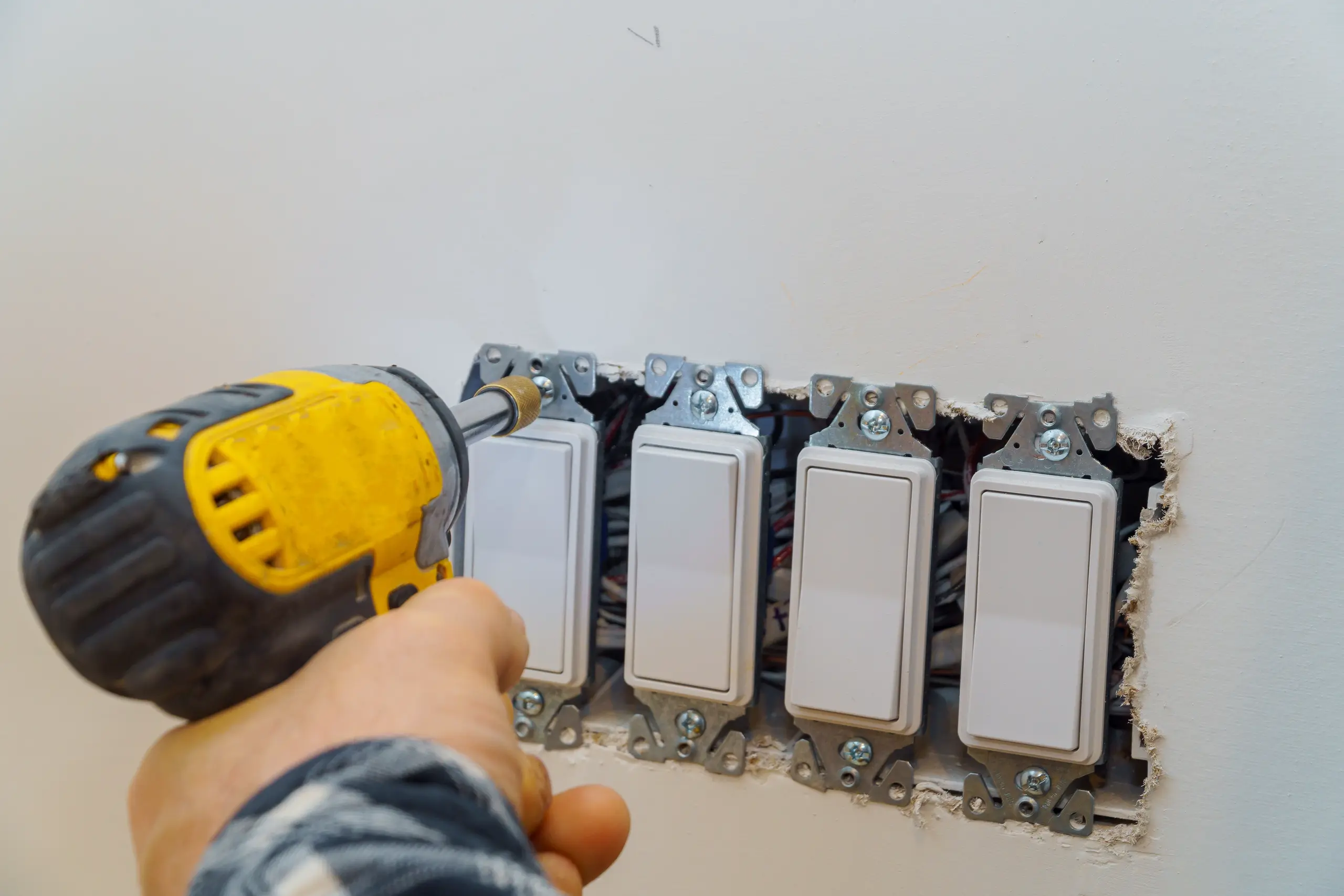 Hand using cordless drill to mount five light switches into wall during Electrical installation