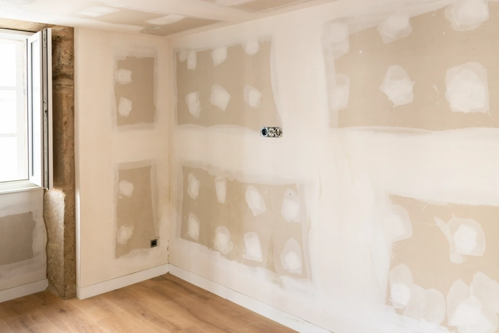 Room interior showing taped and mudded drywall panels and new wood floor ready for Drywall