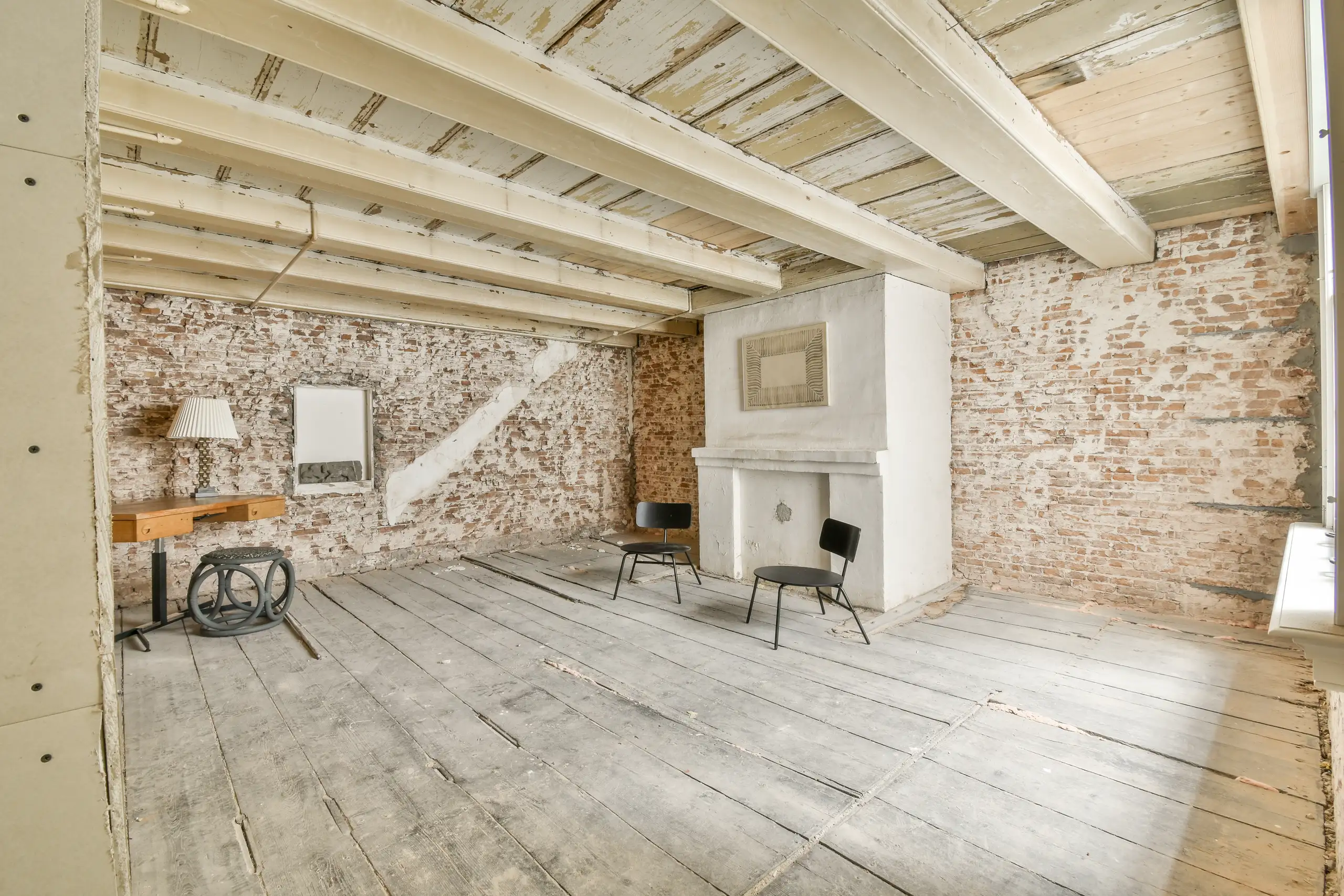 Exposed brick room with stripped wooden floor and beams undergoing Home Renovation with fireplace and minimal furnishings