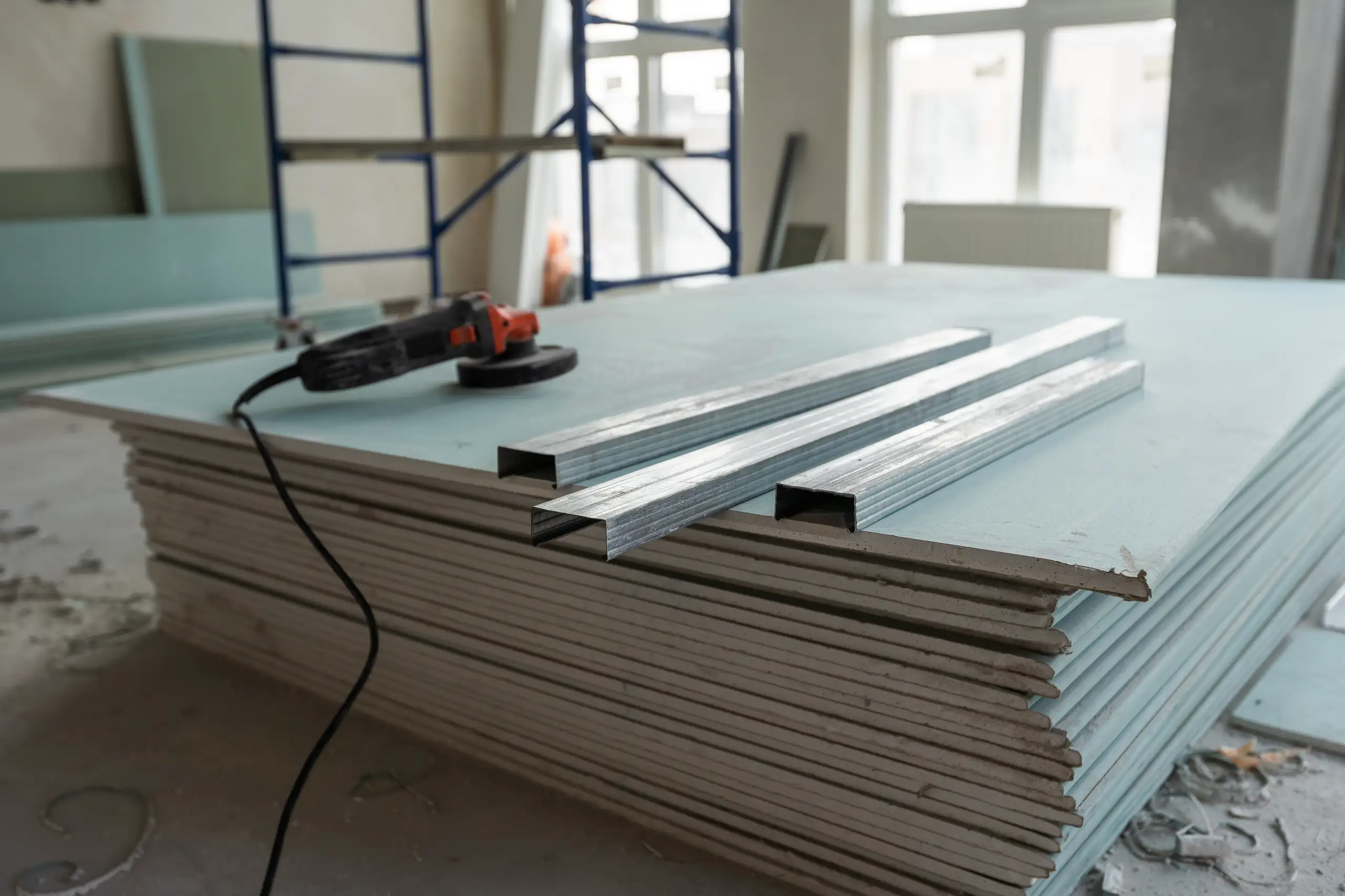 Stack of drywall panels with metal framing channels and angle grinder at renovation site Drywall
