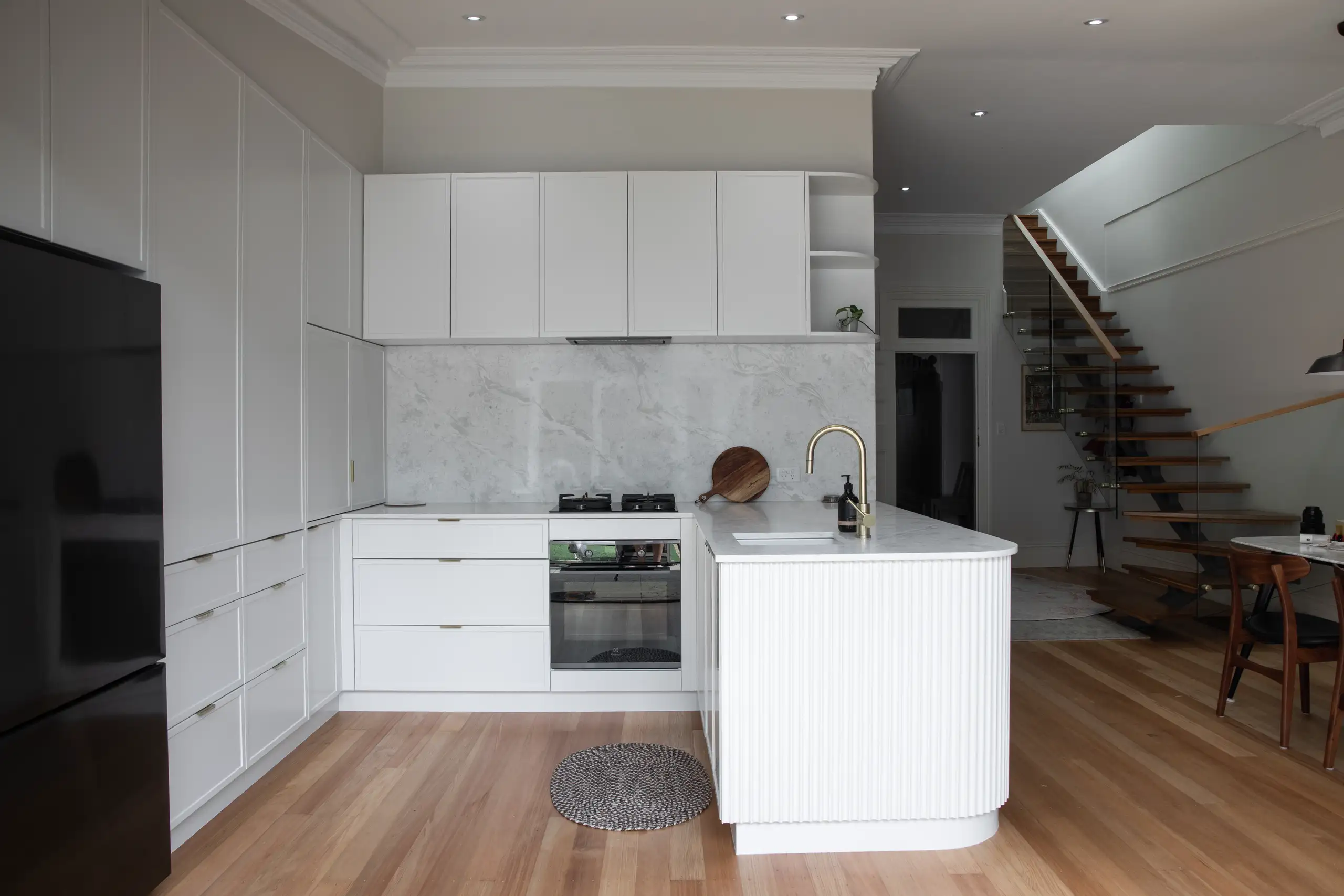 Modern white kitchen with marble backsplash, island, built-in oven, gas cooktop and black refrigerator, Custom Kitchen Remodel