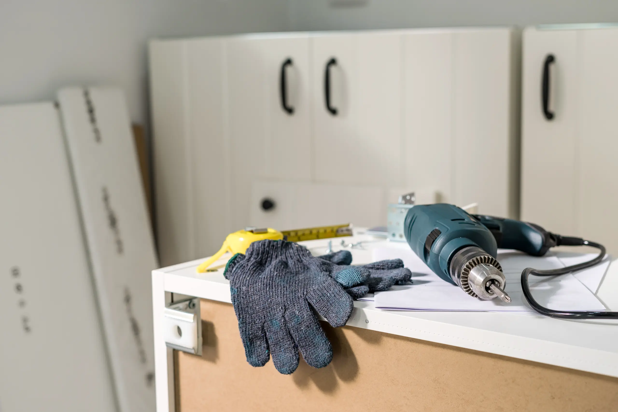 Work gloves, measuring tape and electric drill on partially assembled kitchen cabinet during Kitchen Cabinets Installation