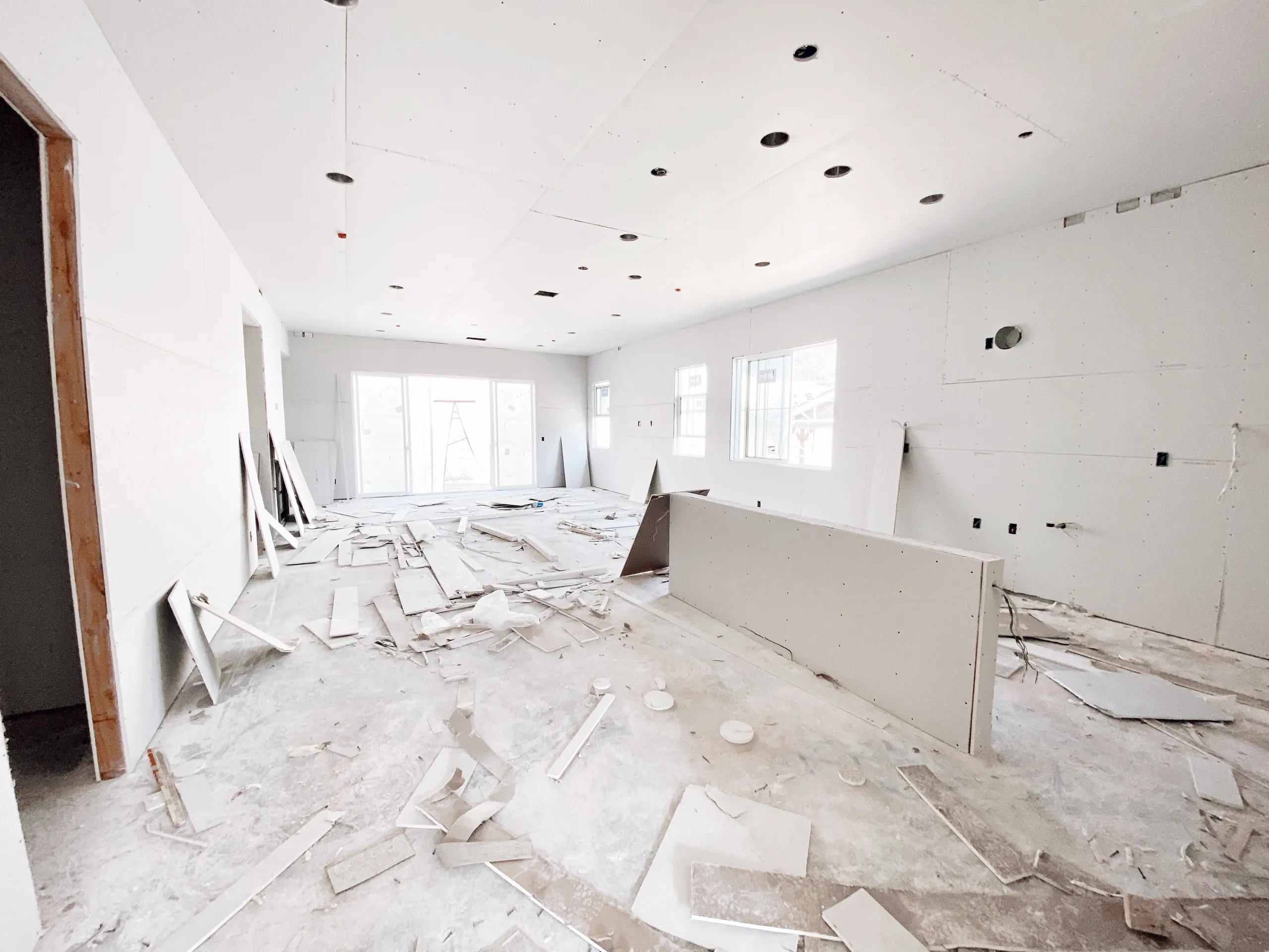 Open residential room under renovation with fresh drywall panels on walls and ceiling and construction debris on floor Drywall
